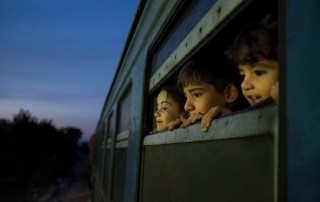 Photo: Children look out a train window at a reception centre for refugees and migrants in the former Yugoslav Republic of Macedonia.