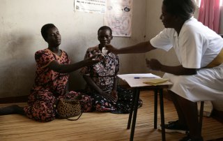 Photo: Two HIV-positive women in Uganda sit on the floor while a Registered Nurse (RN) gives them anti retroviral drugs (ARVs).