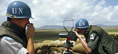 Peacekeepers standing near sand bags and one peacekeeper looking through binoculars.