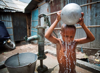 photo of a boy standing in front of a well tipping a bowl of water over his head