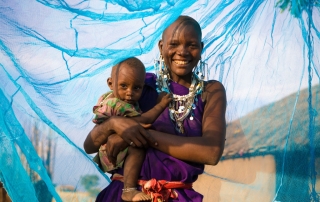 一位面带微笑的母亲抱着自己的孩子在防虐蚊帐里。儿基会图片/Hallahan