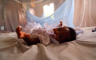 Photo: An infant is surrounded by a malaria bed net in Ghana.