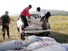 Des travaileurs humanitaires déchargent un camion de vivres sous la surveillance d'un militaire