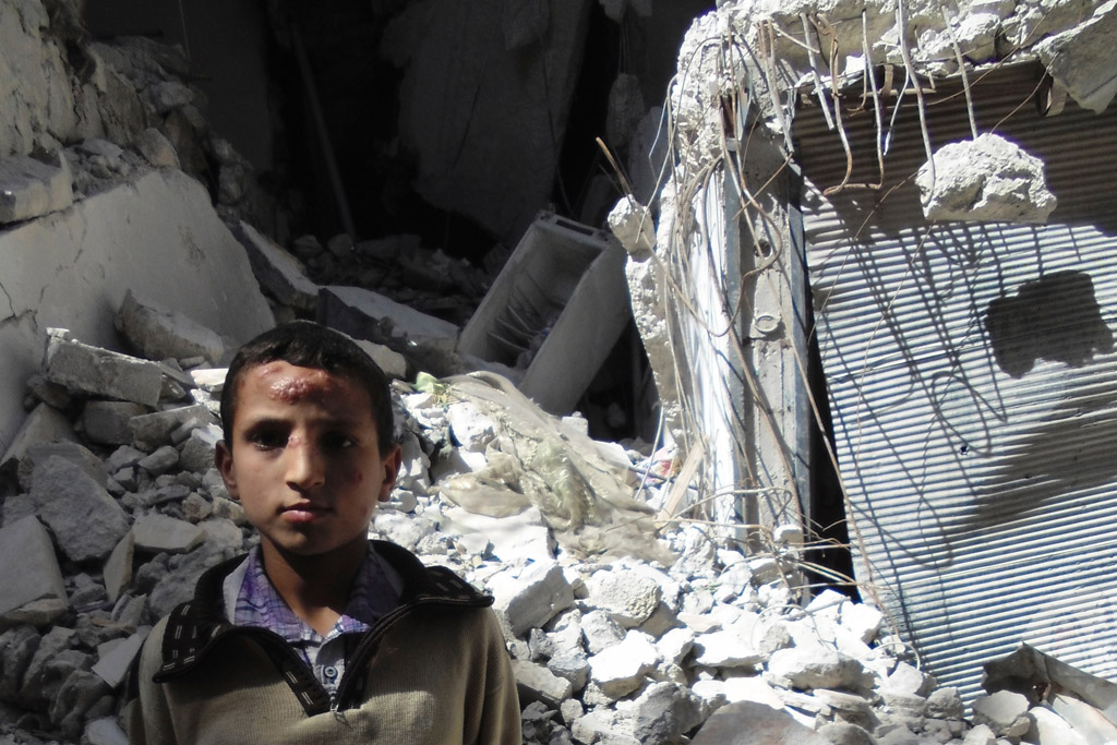 A boy stands outside a building damaged during fighting in Aleppo City, Syria. Photo: OCHA/Gemma Connell