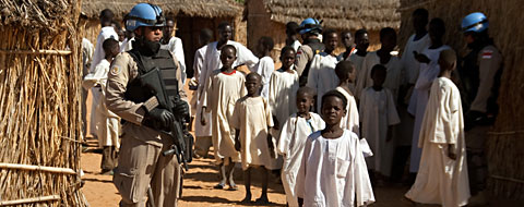 A peacekeeper in uniform standing with children in a camp.