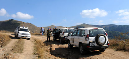 UN peacekeepers inspecting roads near three UN vehicles.