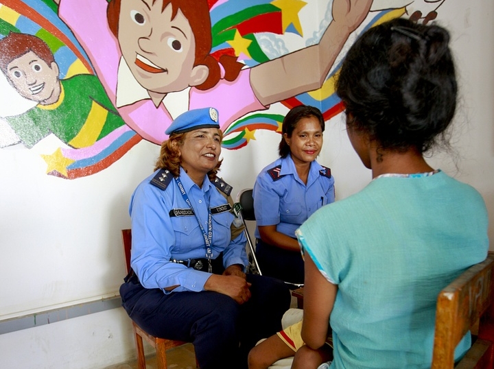 Two UN officers sitting down with a mother and child.