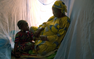 امرأة مع طفلها تحتمي بخيمة مصممة لتقي من الحشرات الناقلة للملاريا