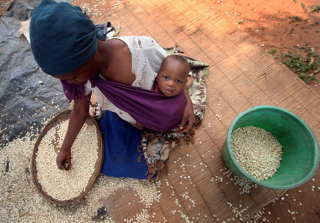 Una mujer con su bebe limpiando granos de maíz en las cercanías de Chimoio, Mozambique. Foto: FAO