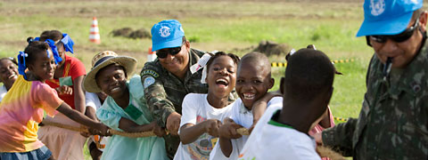 Dos miembros del personal de paz participan en un juego de tira y afloja con un grupo de niños.