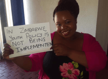 A young woman holds a sign that says, "In Zimbabwe, youth policy is not being implemented"
