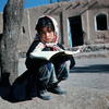 Young girl reading in a copy book, street scene, child revising lesson, reading