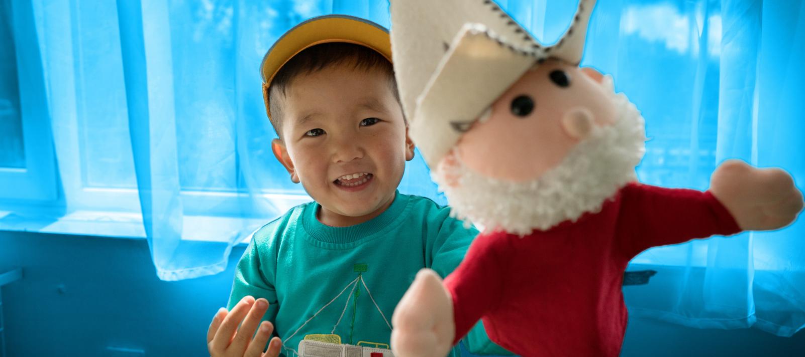 Smiling boy holds soft toy up to camera in Kyrgzstan.