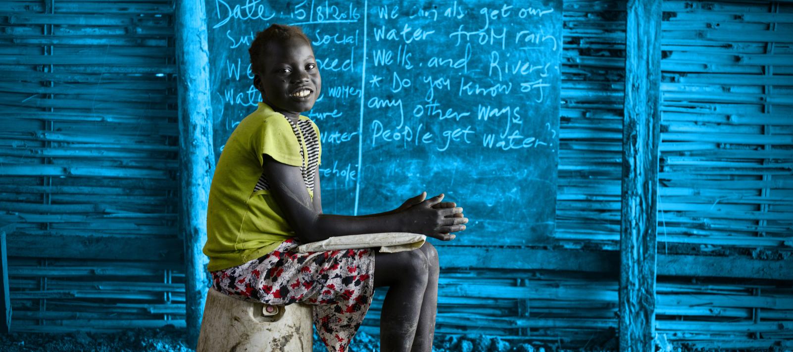 A girl sits in front of a chalkboard, South Sudan