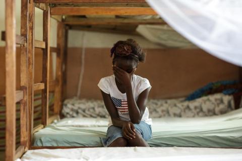 A girl sits on a bed with her head in her hand, Sierra Leone