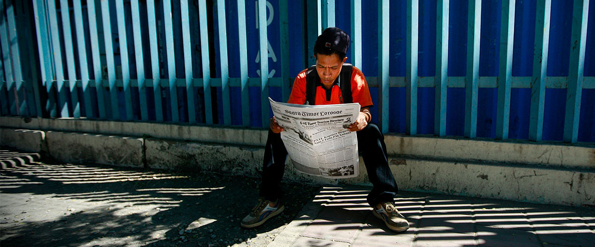 Young man reading newspaper in Dili, Timor-Leste. Photo by Martine Perret