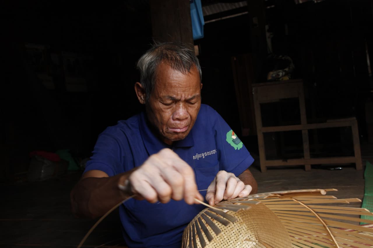 Jarai elder weaving strips of bamboo to make a basket.