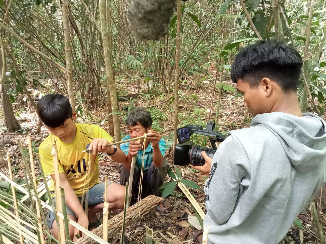 Indigenous youth documenting a Brao father and son preparing a trap made of strips of bamboo. 