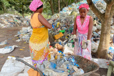 Picture of two women next to a plastic collection point putting plastic bottles into a wheelbarrow