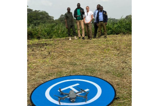 4 men standing in background piloting a drone. Drone on foreground on take off/landing piste