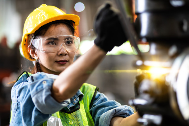 A women engineer, wearing a safety helmet and glasses, is operating a machine