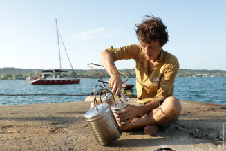 Picture of Corentin de Chatelperron holding a plastic pyrolyzer, with the sea and a sailboat in the background