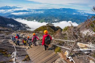 Hikers wearing helmets walk down the slope, high above the clouds and an impressive landscape