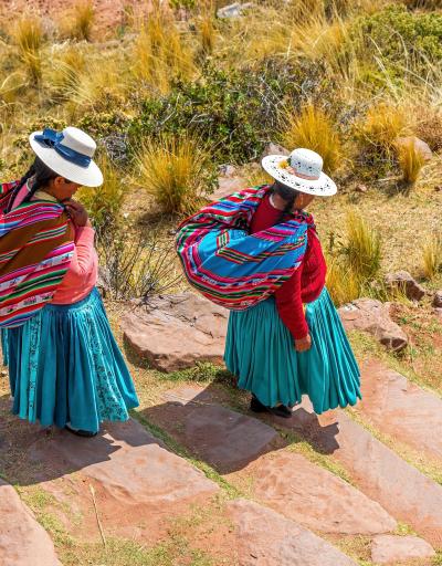 Two Quechua indigenous women in traditional clothing and textile walking down steps, Taquile island, Titicaca Lake, Puno, Peru.